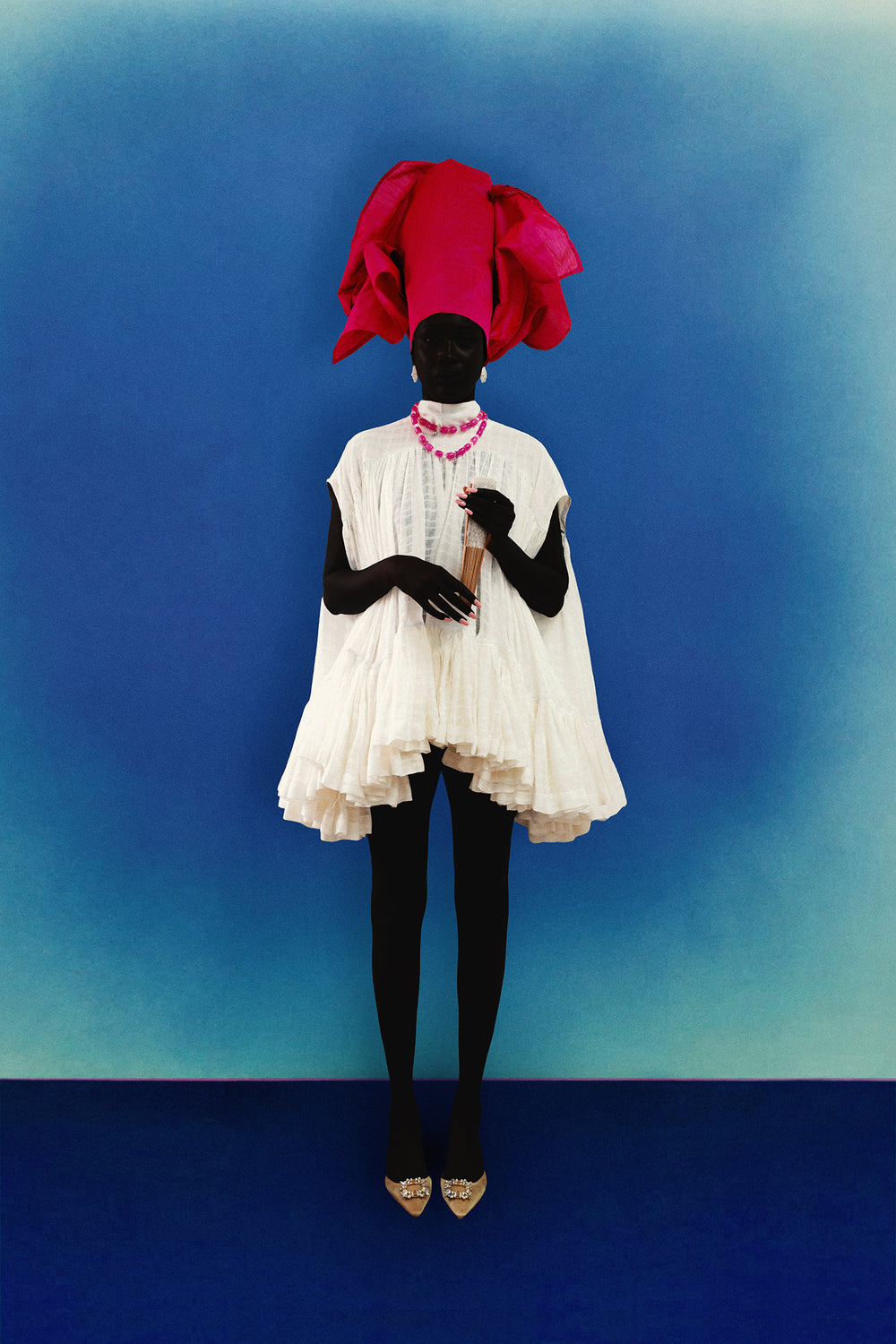 Person wearing a white cotton maison kébé Oceane dress with a magenta red headscarf against a blue background